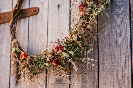 Close up photo, part of twisted crafting, natural creative dry herbal wreath from twigs of wild flowers, cereal and grass. Traditional festive ethnic decoration on entrance door. Thanksgiving dayの写真素材