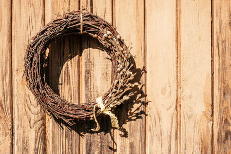 Tightly woven hanging willow wreath from wickers with decorative cotton twigs and white tape lace. Rural yellow wooden and planking wall on background. Traditional seasonal decoration. Copy spaceの写真素材