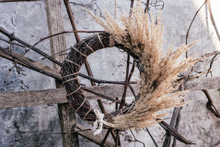 Dry herbal twig, tightly woven wreath with twisted cereal and white ribbon. Rustic gray stone wall and planks on background. Ritual and ethnic tradition. Symbol of defense. Shadow side. No peopleの写真素材