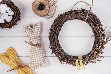 Easter crafting woven willow wreath with tape bow. White planking wall background. Eggs nest and toy rabbits invitation. Tradition festive seasonal decoration step by step. Workshop ornament. Top viewの写真素材