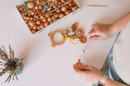 Natural safe accessories of wood on white desk, eco style. String beads. Ecological teether toy with...