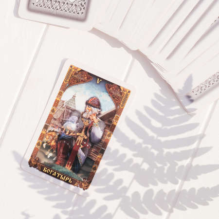 Deck of Tarot cards fanned out on white board surface with open card with inscription Hero in russian and fern leaf shadow. top view. Square image. Minsk, Belarus - 28.07.2021のeditorial素材