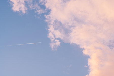 Background image of blue bright sky with pastel pink and white clouds and airplane with trail....