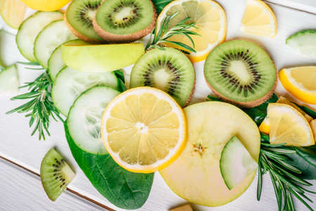 Partially blurred green and yellow fruits and herbs cut into pieces lie on white table. Ingredients...