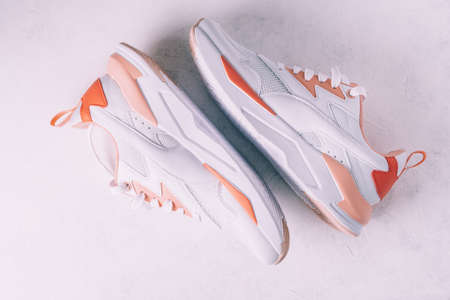 White womens sneakers with coral inserts on white concrete background. Top view. Flat lay.