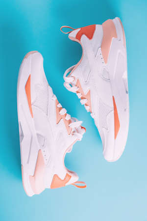 White womens sneakers with coral inserts on blue background. Top view. Flat lay.
