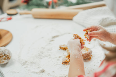 Partially blurred hands of little girl in red checkered shirt prepare dough for gingerbread cookies in white kitchen. Child knead dough on white table strewn with flourの写真素材