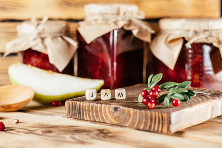 Jars of homemade lingonberry and pear jam with craft paper on lids on wooden surface next to fresh lingonberries and pears.の写真素材