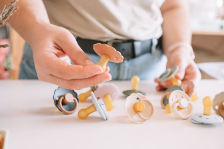 Cropped business woman hands, making and design craft silicone pacifiers for newborn babies on white desk. Small business, store. Choosing soft material for kids. Natural ecological accessories.の写真素材
