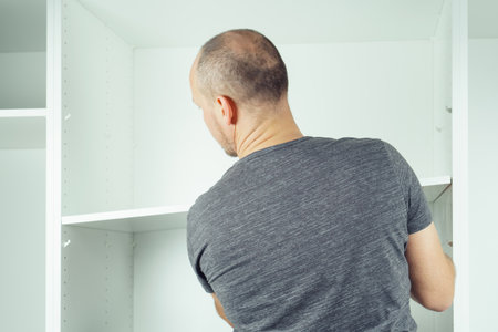 Male hold shelf, inserting and securing it to supports, assembling white dresser or wardrobe. Self-assembly of furniture at home, DIY, furniture repair and rearrangementの写真素材