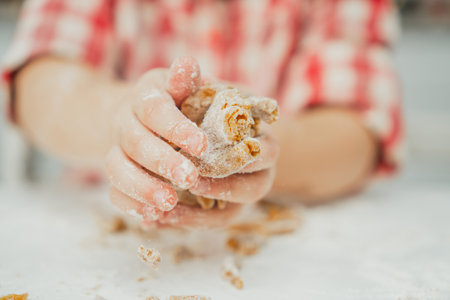 Partially blurred hands of little girl in red checkered shirt prepare dough for gingerbread cookies...