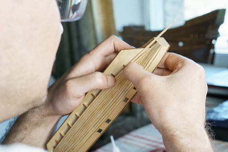 Hands of man gluing plywood details for ship model with glue, holding with fingers. Process of...