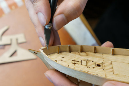 Hands of man cutting out details for ship model with clerical knife from plywood. Process of...
