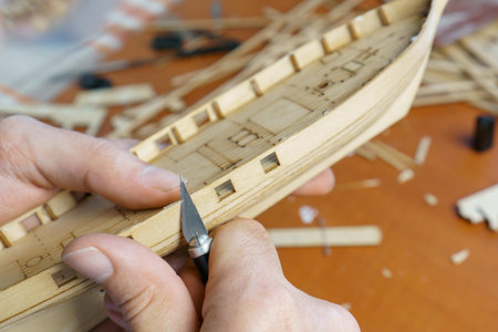 Hands of man cutting out details for ship model with clerical knife from plywood. Process of...