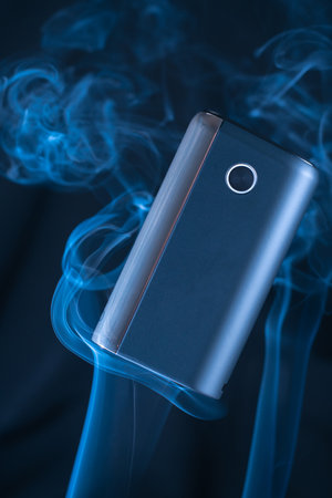 Black new GLO heating smoking device floats in puffs of white blue neon smoke. Modern electronic...