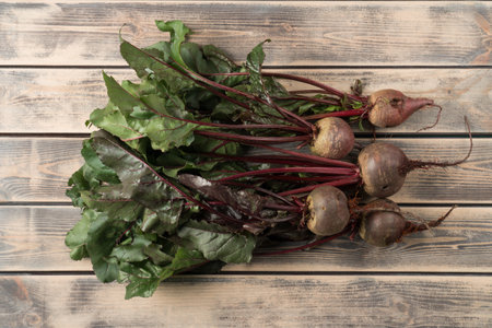 Bunch of fresh ripe beets with long green haulm on faded wooden table, top view. Prepare unpeeled...