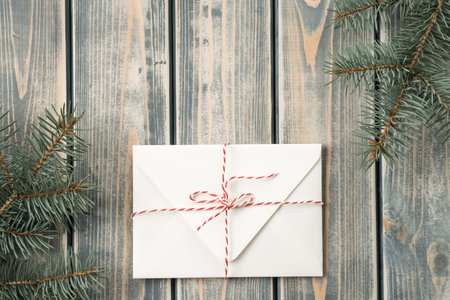 White envelope on gray wooden background with branches of Christmas tree. New year envelope tied...