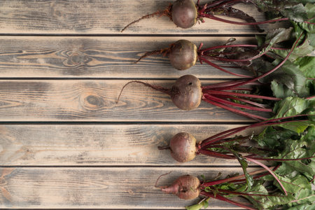 Layout of fresh, clean purple beet roots with stems and leaves on wooden background. Diet and...