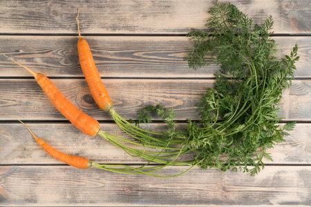 Orange tasty juicy carrot with green stem and leaves on wooden background. Healthy lifestyle, good vision and carotene vitamins in organic farm food. Diet and healthy lifestyle. Top view, copy spaceの写真素材