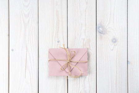 Pink envelope tied with rough jute rope on white wooden background. Copy space. Top view. Mail, correspondence, sending messages, congratulationsの写真素材