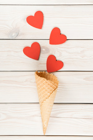 Vertical shot of hearts moving from waffle cone like confetti on light wooden background. Ice cream dessert and other sweets as present on saint Valentines Day. Love and romance. Copy space, flat layの写真素材