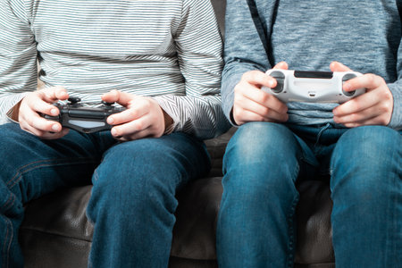 Male hands hold modified plastic joysticks. Friends play videogames sitting on couch. Two people hold wireless game console. Press buttons on controller by fingers. Modern technologies and gaming.の写真素材