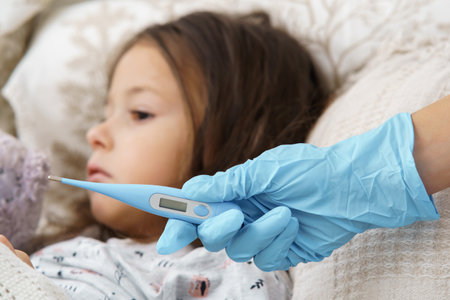 Cropped doctor hand in glove holding electronic thermometer against calm, sad, silent little girl....