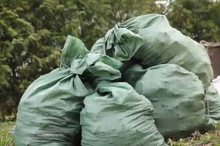 Pile of green plastic free ecological trash bags on dump outdoors. Segregation, sorting and...