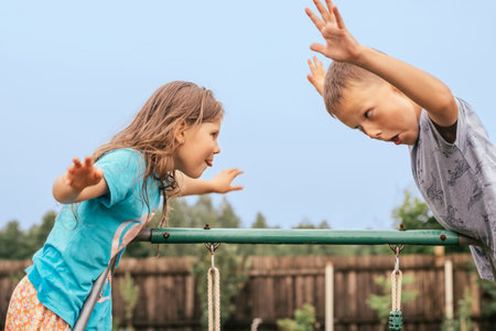 Cheerful little girl and boy fool and make faces standing opposite. Friends have fun on the playground. outdoor walking. Funny facial expressions. Summer vacation, childhood, street lifestyle.の写真素材