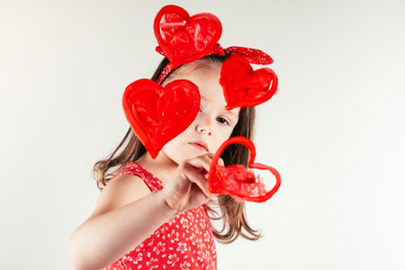 Pretty little girl carefully draw red hearts with paintbrush on invisible wall. portrait of child on white. Drawing, creative present. Saint Valentine's Day concept, holiday of all lovers.の写真素材