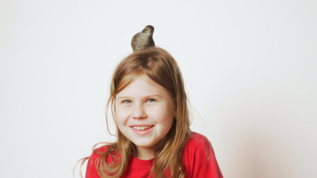 Grown up starling nestling sitting on head of glad little girl. Portrait of a happy child on white....
