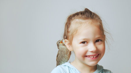Grown up starling nestling sit on shoulder of little girl and sing with open beak. Portrait of happy...