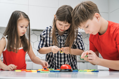 Portrait of group of focused friends children standing at table in kitchen at home, playing board...