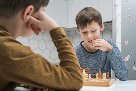 Portrait of two concentrated preteen boys friends brothers sitting at table in bright kitchen at...
