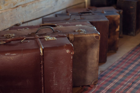 Row of antique shabby suitcases on floor of wooden countryside house. Brown leather old fashioned baggage for travelling. Storage of worn junks indoor. Big closed vintage packed bags.の写真素材