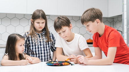 Group of friends play toy fishing on kitchen table. Smart boy hold fishing rod and pick up playthings from plate. Home leisure, funny playtime. Entertaining interesting board game.の写真素材