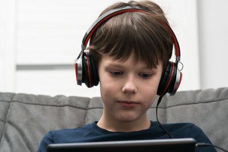 Portrait of little boy with digital tablet computer. Child in wired headphones play videogame on gadget or listen to music. Online entertainment, home leisure, gamer, modern electronics.の写真素材