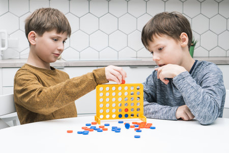 Two positive, pensive and concentrated little boys playing connect four game 3d with yellow plastic field with holes for figures on white table. Tactic and education with games. Home entertainmentの写真素材