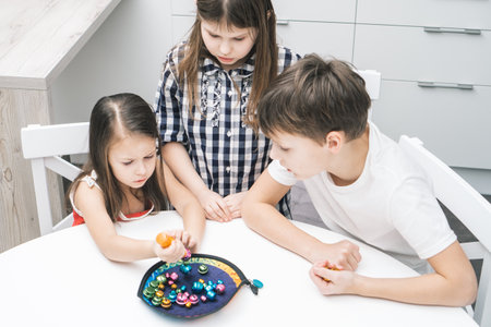 Cloudy looking children of girls and boy looking at girl trying to catch fish bell from fish plate like fisherman. Fish rod games for motor and memory skills. Child development center, day careの写真素材