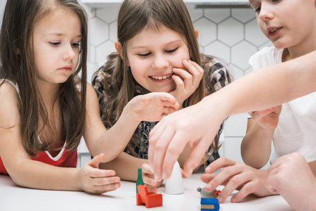 Smiling, concentrated children playing with furniture toys on white table. Chair, bottle and other plastic toys for fun. Imagination and creative games for kids. Role play and new ideas for playingの写真素材