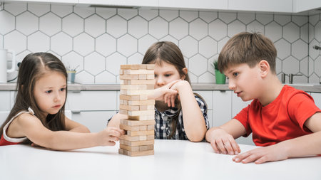Thoughtful and concentrated kids playing balance wooden brick tower game, building pyramid on table. Educational ecological games at home. Architectural skills and spatial analysis developmentの写真素材