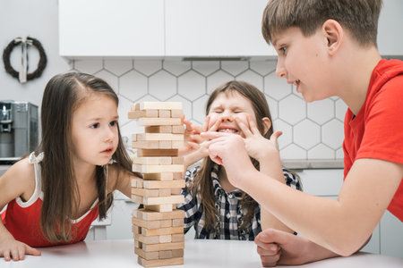 Nervous and worried, passionate kids playing board balance wooden brick tower game together. Little boy trying to move wooden cube out of tower line. Children competition, training in stability puzzleの写真素材