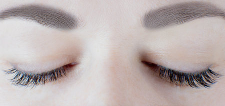 Close-up of closed eyes with long false eyelashes, black eyeliner, flawless skin, gorgeous eyebrows of unrecognizable young woman. Macro shot. Beauty procedures, cosmetology, microblading, make-up.の写真素材