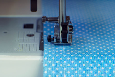 Close up sewing machine steel part with needle, pressure foot stitching with thread on blue fabric, textile. Dressmaker or tailoring industry, workshop and atelier. Needle craft and manufacture workの写真素材