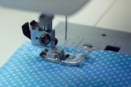 Macro shot of sewing machine steel pressure foot with needle and thread making stitches on blue fabric polka dot fabric. Tailor and dressmaker shop, atelier, dressmaker industry. Clothes makingの写真素材