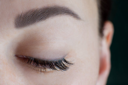 Close-up of brown eye with beautiful long eyelashes, black eyeliner, ideal skin, eyebrow of unrecognizable young woman looking down. Macro. Eyelash extension, beauty procedures, make-up. Soft focus.の写真素材