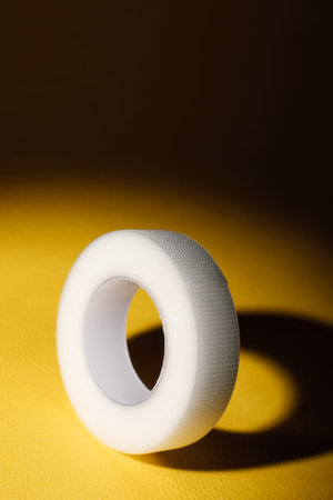 Flexible plastic tape for eyelash extension procedure, illuminated from above, lying on yellow table. Tool with durability, ensuring lashes remain properly positioned throughout procedure. Vertical.の写真素材
