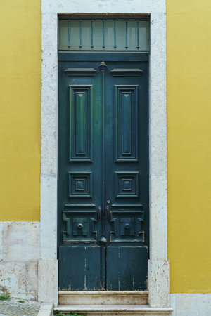 Ornate old high green wooden door of yellow stone building house with white frame decorated with forgings carvings ornaments with peeling paint. Architecture, historical buildings, vintage. Vertical.の写真素材
