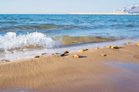 Beautiful view of wet sand, beach seashore coastline, foamy sea waves, stones on sunny windy day. Summer, holiday, vacation, travelling, tourism, seascape ocean, wallpaper, advertisement.の写真素材