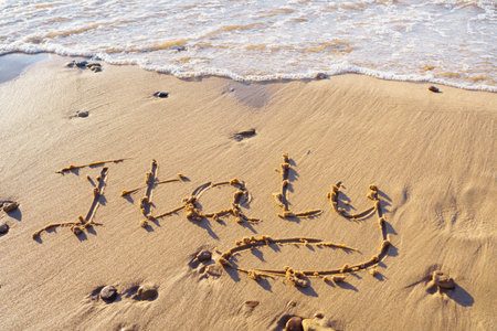 Close-up of inscription word Italy written on wet sand of beach seashore coastline after tide near sea waves on sunny day. Summertime, holiday, vacation, travelling, seascape, tourism, handwriting.の写真素材